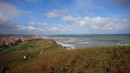 A view from a hill next to the sea with sea and houses visible.
